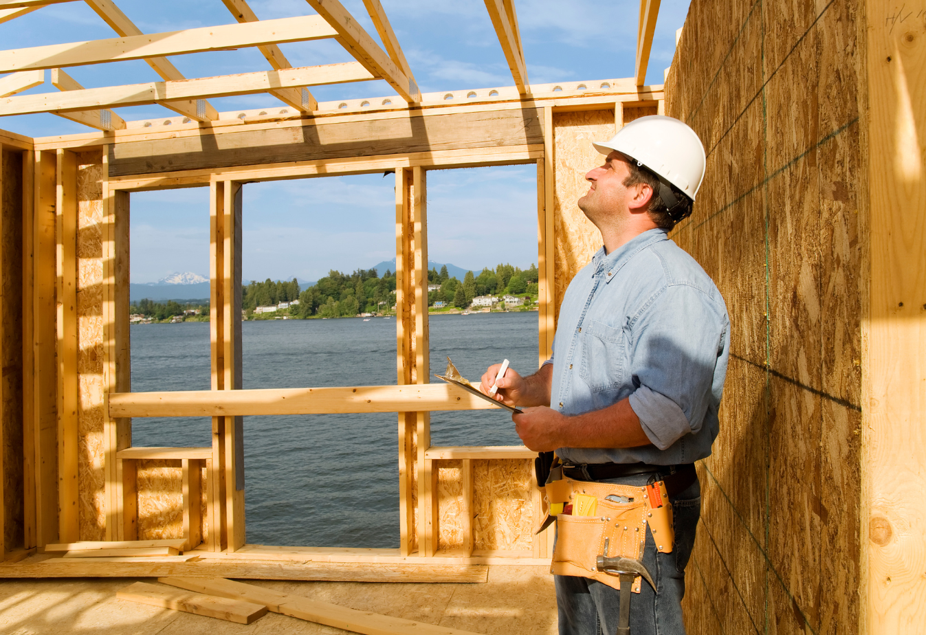 a man in a white hard hat surveys a wooden structure that will become a house