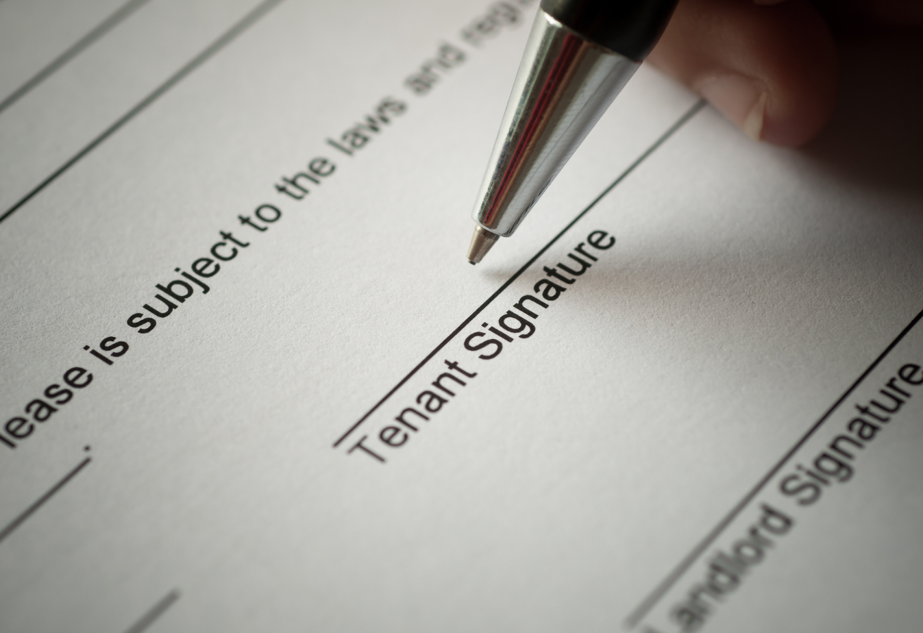 the point of a pen hovering over a document line that reads "tenant signature"